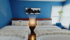 Habitación doble con una cama y una obra de arte urbana sobre ella, una mesita de noche con lámpara y una ventana con persianas.