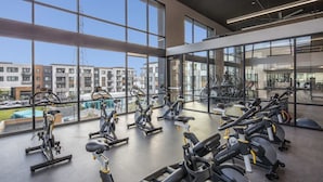 A gym with stationary bikes and treadmills, large windows, and a view of buildings. - Luxury 1BR Condo in Silicon Valley's Heart (Menlo Park)