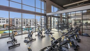 A gym with stationary bikes and treadmills, large windows, and a view of buildings.