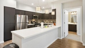 A modern kitchen with dark cabinets, stainless steel appliances, a white island, and pendant lighting. - Luxurious Silicon Valley Condo: Rooftop Lounge and Pool (Menlo Park)