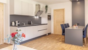 Una cocina moderna con armarios blancos, encimera oscura y un comedor con mesa y sillas.