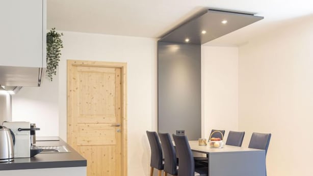 Una cocina compacta con electrodomésticos modernos, un comedor con mesa y sillas, y una puerta de madera.