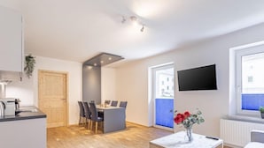 A modern apartment with a kitchen, dining area, and living space. It features a wooden dining table, a small wooden coffee table, and a TV mounted on the wall. - für 5 P. mit IR-Sauna & Sprudelwanne by Interhome (Eisenerz)