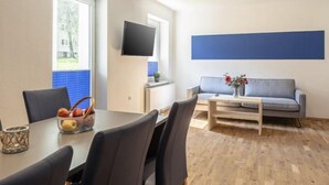 A modern living room with a dining area, a flat-screen TV mounted on the wall, a grey sofa with a vase of flowers, and a wooden coffee table. - für 5 P. mit IR-Sauna & Sprudelwanne by Interhome (Eisenerz)