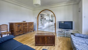 Sala de estar con un mueble de madera, televisor, sofá y un área de comedor visible a través de un arco.