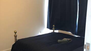 A bedroom with a bed, a nightstand, a window with curtains, and a wall-mounted light fixture.