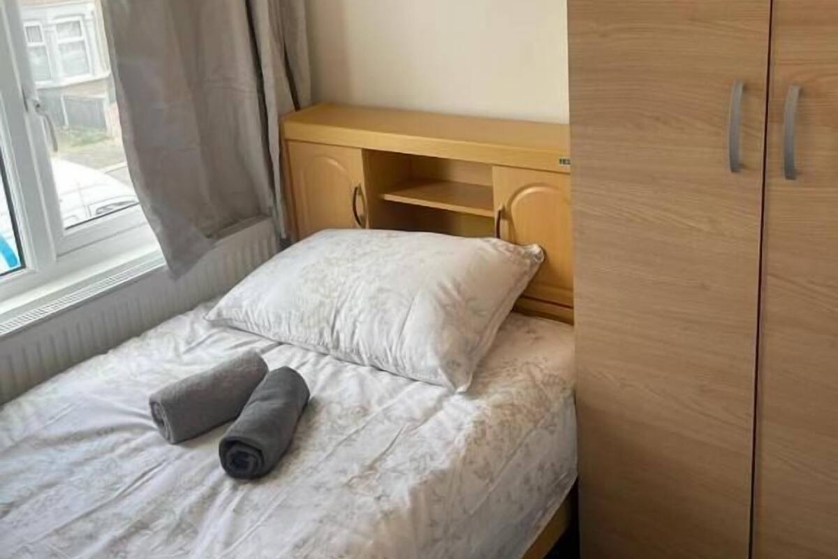 A single bed with a patterned duvet, a pair of rolled towels, and a wooden wardrobe with two doors.