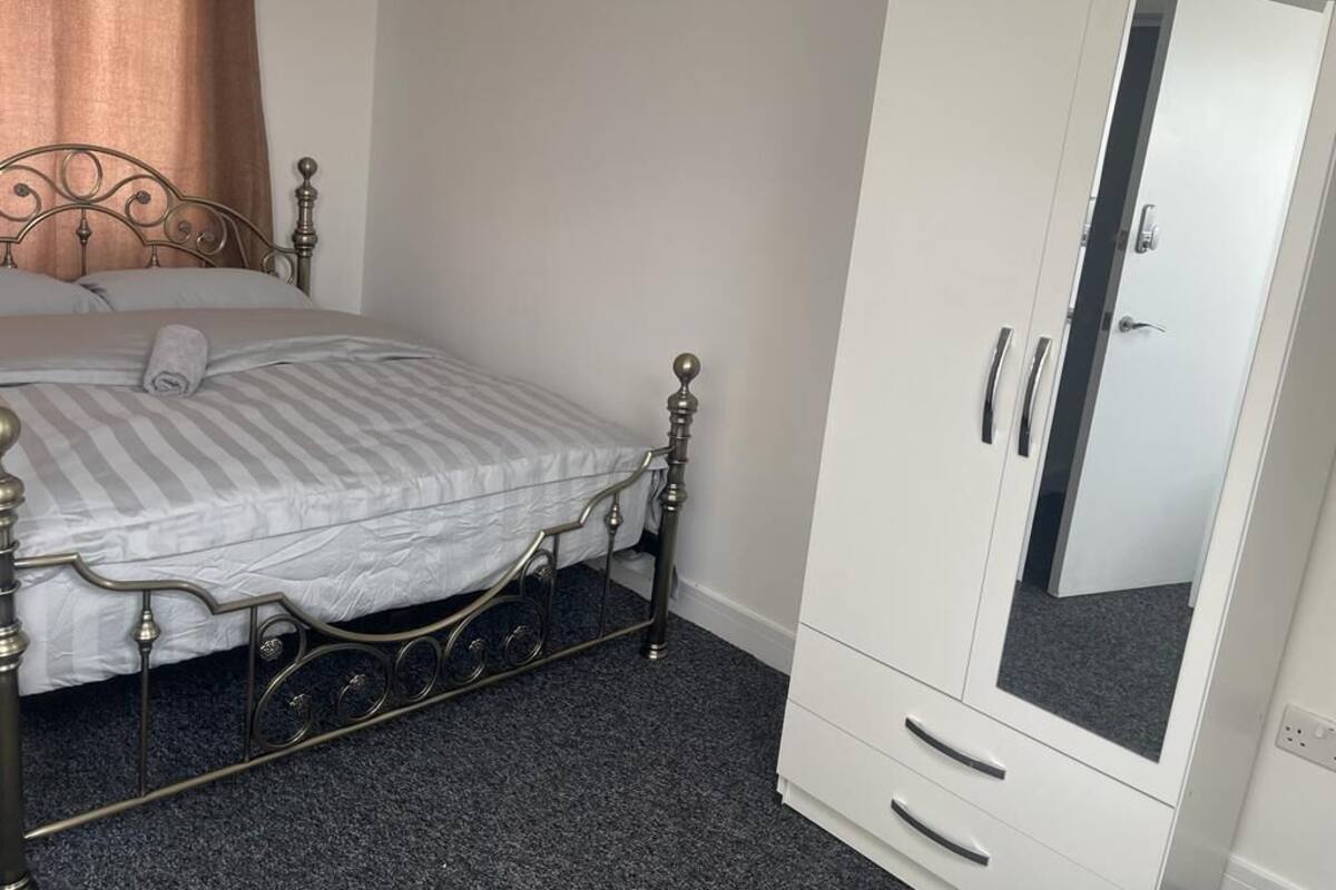 A bedroom with a metal-framed bed, a white wardrobe with a mirror, and a grey carpet.