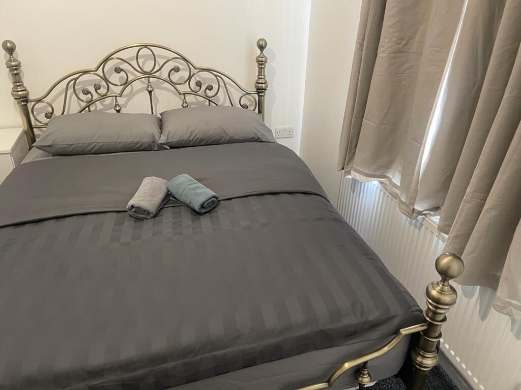 Een net opgemaakt bed met een donkergrijze dekbedovertrek en kussens, een metalen hoofdbord en een raam met gordijnen.