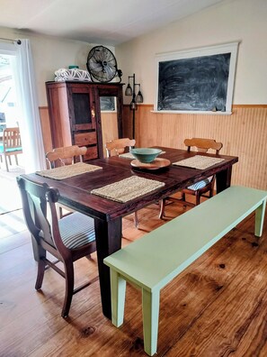 Ein Essbereich mit Holztisch, Stühlen, einer Bank, einem Ventilator, einer Tafel und einem Fenster.
