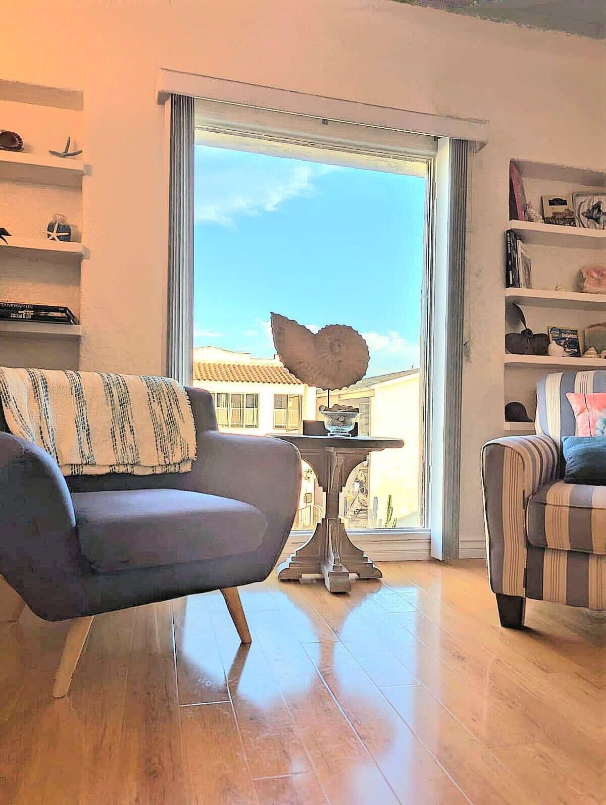 Un soggiorno con divano, un tavolo con una ciotola decorativa e vista su un edificio attraverso un'ampia finestra.
