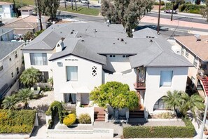 A two-story house with a flat roof, satellite dishes, and a small garden with palm trees. - The Dolphin: Beach~Workspace~W/D incl~PetsOK (Long Beach)