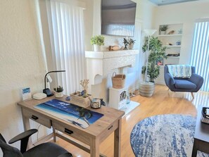 A modern living room with a wooden dining table, a blue rug, a grey armchair, and a white fireplace mantel with decorative items.
