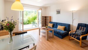 Ein modernes Wohnzimmer mit Glastisch, blauem Sofa, Holzsesseln und einer Stehlampe.