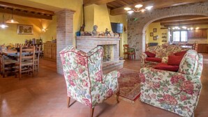 A spacious living room with a fireplace, floral armchairs, and a dining area with wooden furniture.