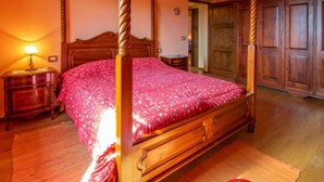 A four-poster bed with a floral bedspread in a room with wooden furniture and a wooden floor.