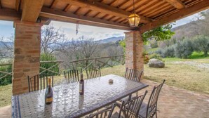 A covered outdoor dining area with a table and chairs, a bottle of wine, and a lantern.