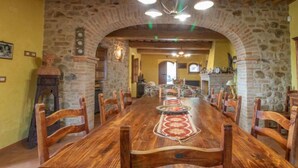 A rustic dining room with a long wooden table, stone walls, and a stone fireplace.