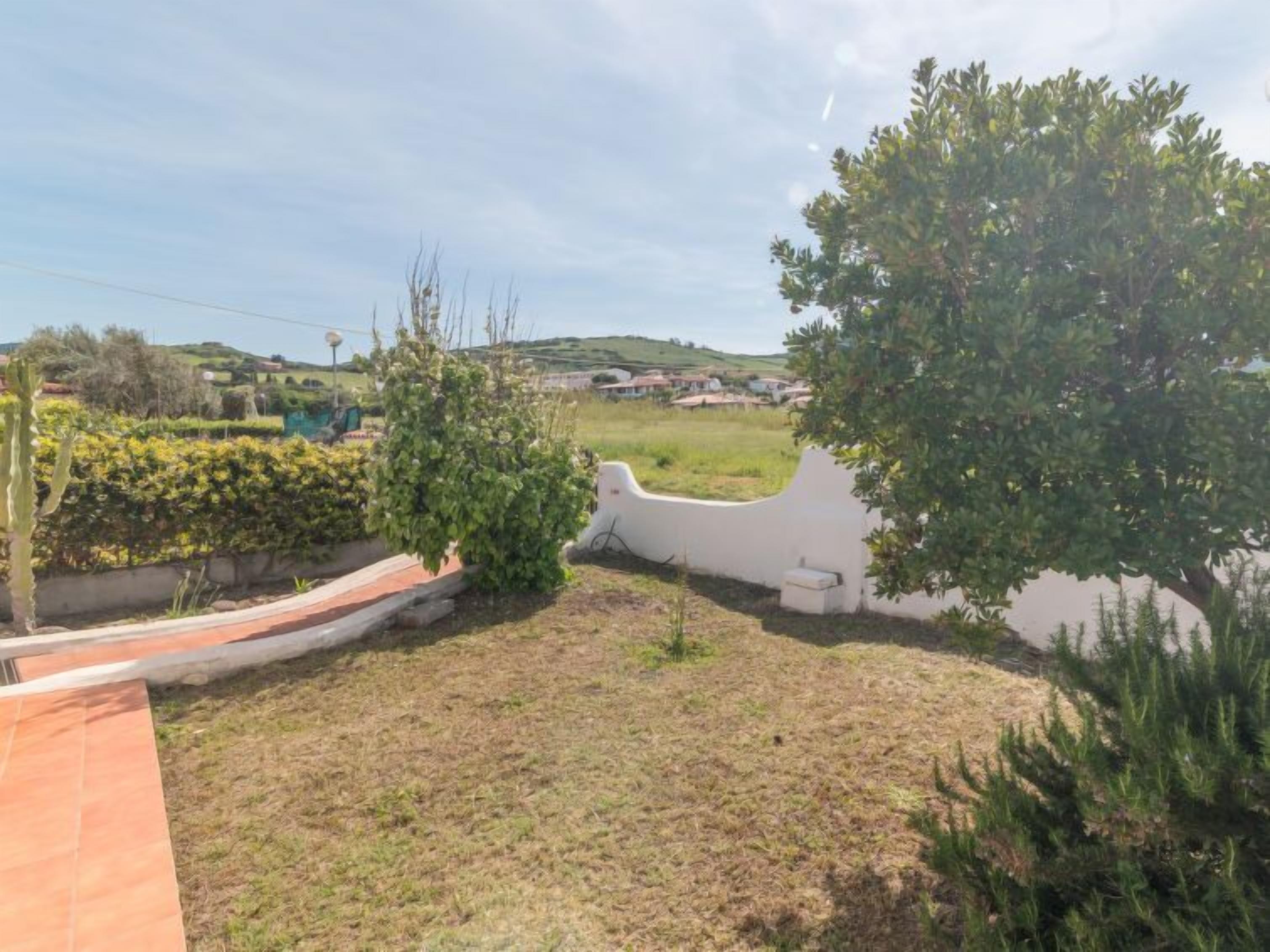 A residential area with a paved pathway, a white wall, and a grassy field.