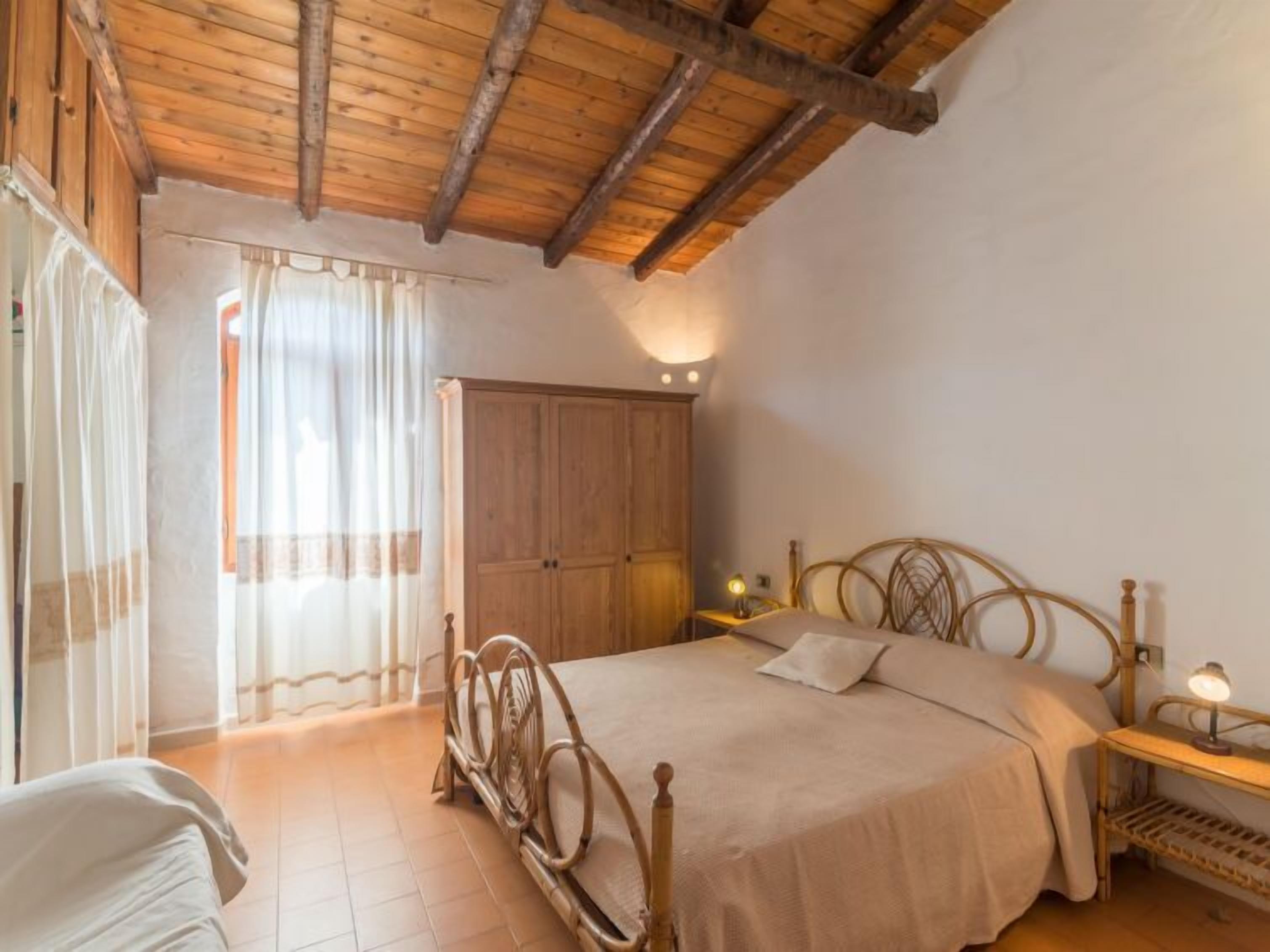 Camera da letto con soffitto in legno, un letto con testiera, un armadio e un comodino con lampada.
