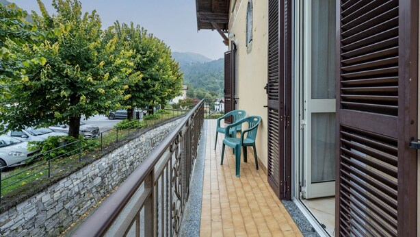 A balcony with a stone wall, a view of parked cars, and a tree. - Apartment Adele by Interhome (Bee)