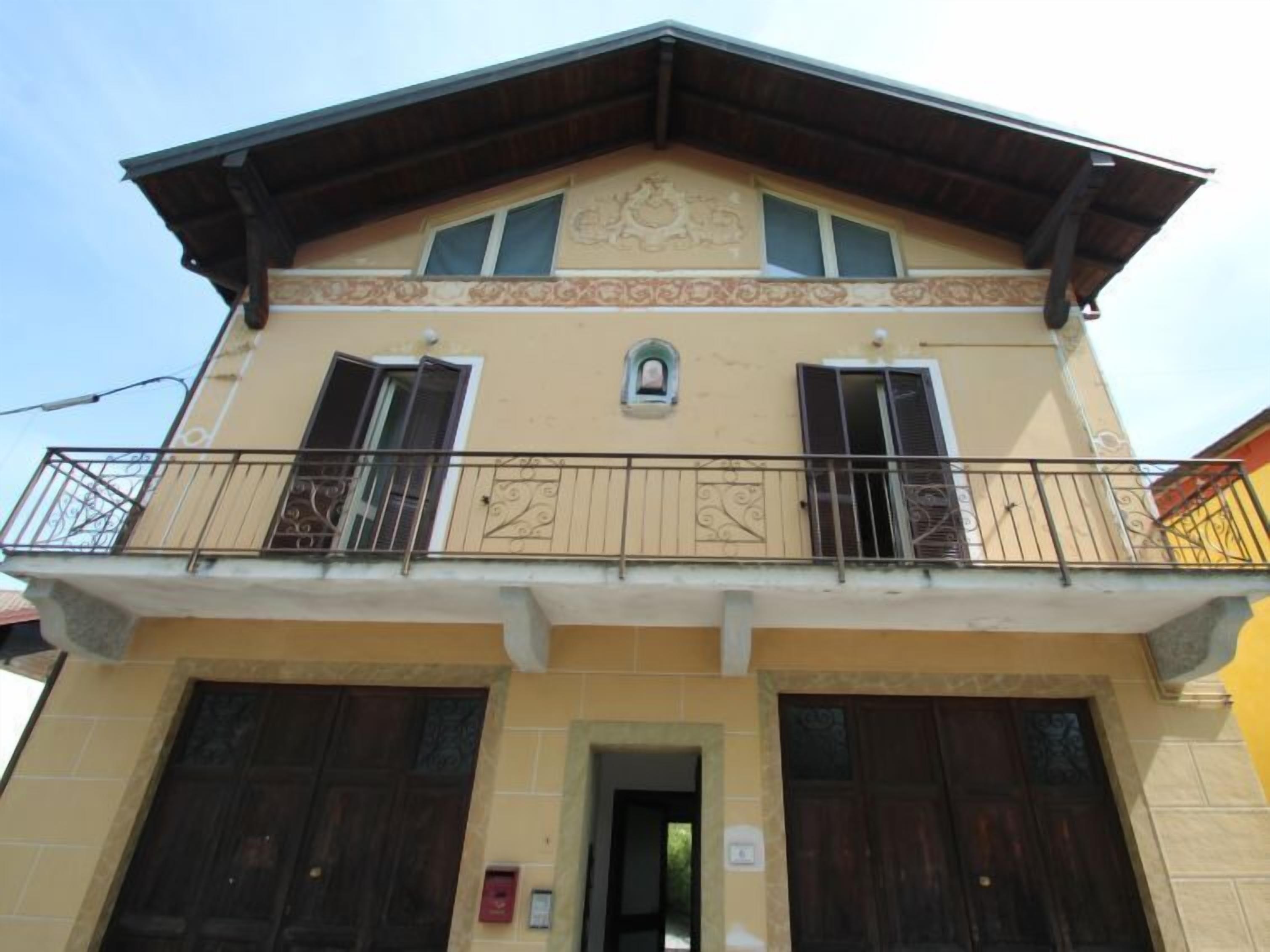 A two-story building with a balcony, large wooden doors, and a small window with a decorative element above it.