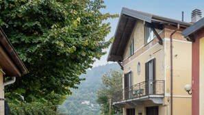 A street view with a building featuring a balcony, a stone wall, and a mountain in the background. - Apartment Adele by Interhome (Bee)