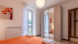 A hotel room with a large bed, a radiator, a window with curtains, a door, and a mirror. - Apartment Adele by Interhome (Bee)