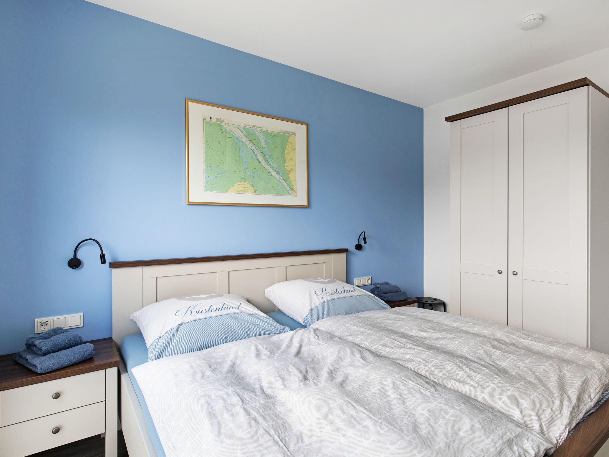 Un dormitorio con cama, mesita de noche, cómoda y un mapa en la pared.