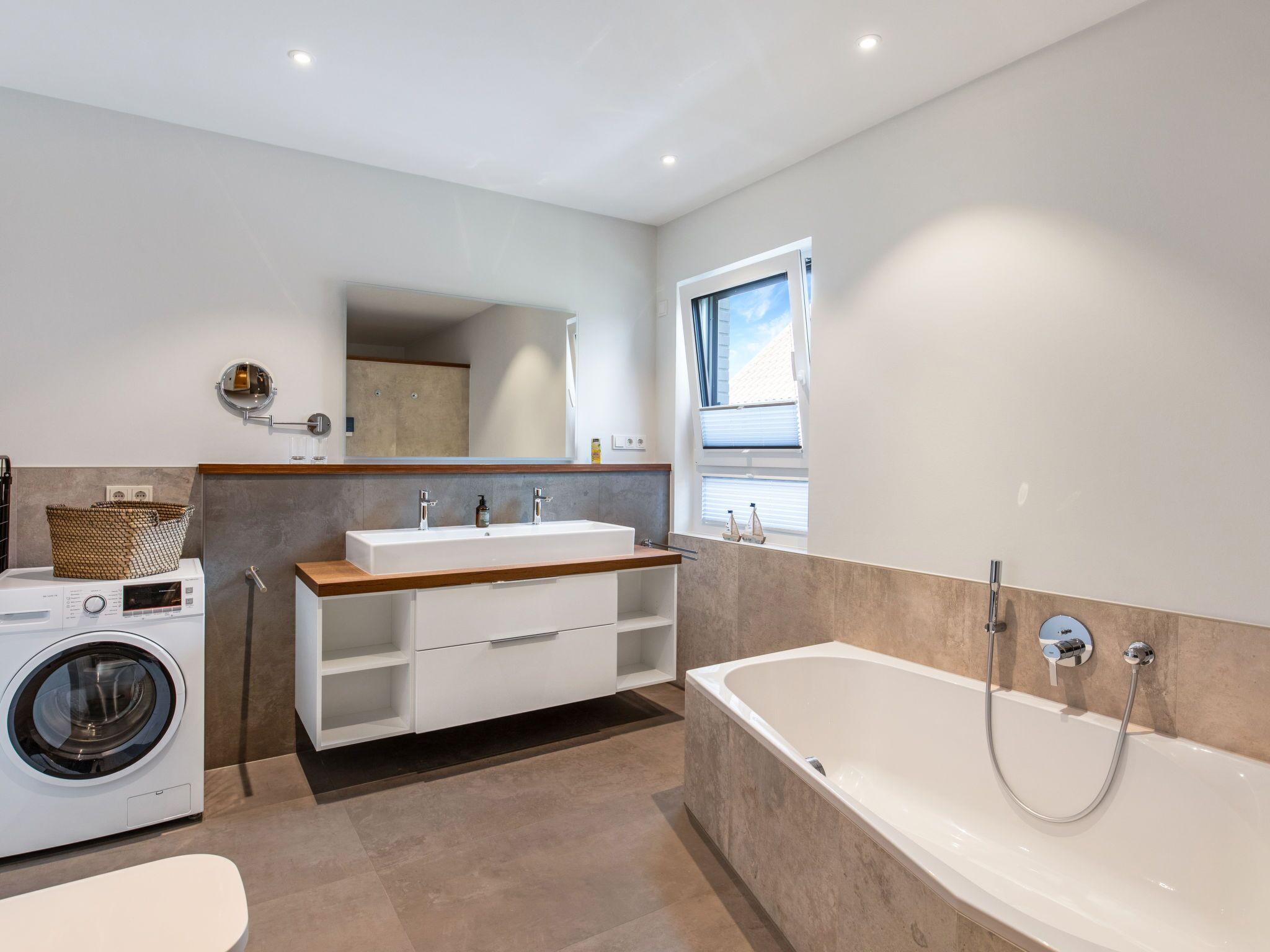 Une salle de bain moderne équipée d’un lave-linge intégré, d  ’une baignoire sur pieds et d’un meuble-lavabo avec miroir.