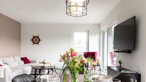 Un coin repas avec une table en bois mise pour le repas, un vase de fleurs et un téléviseur fixé au mur.