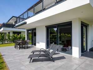 Ett modernt hus med en uteplats, utomhusmöbler och en glasdörr som leder ut till en trädgård.