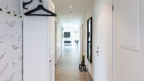 A hallway with a wooden floor, white walls, and a black hanger on a white wall. There is a small stool with a plant on it. - Fischer sien Huus by Interhome (Fedderwardersiel)