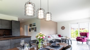 A modern dining area with a wooden table set for four, a kitchen in the background, and a cozy seating area with a sofa and armchairs. - Fischer sien Huus by Interhome (Fedderwardersiel)