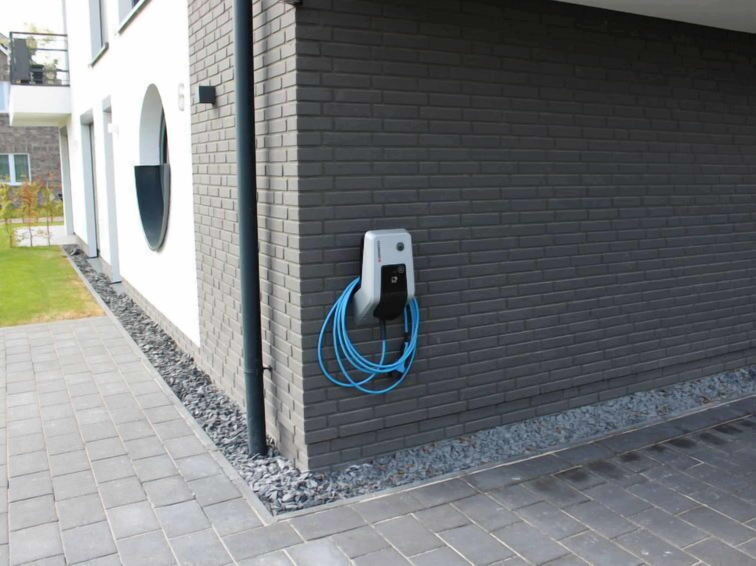 Un edificio moderno con fachada de ladrillo, un sendero pavimentado y limpio, y un cuadro eléctrico con cable azul.