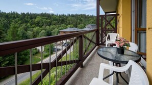 En balkong med ett glasbord och stolar, med utsikt över ett skogsområde.