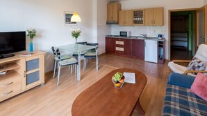 Un espace de vie compact comprenant un téléviseur, une table à manger, des chaises, une table basse avec des fruits, un canapé et une kitchenette.