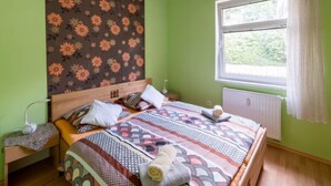 Une chambre à coucher avec un lit, une table de chevet, une fenêtre avec des rideaux et un radiateur.