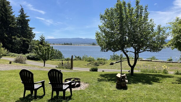 A grassy area with two Adirondack chairs facing a lake.