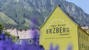Ein gelbes Gebäude mit der Aufschrift "Alpin Resort ERZBERG Eisenerz" und "Urlaubserlebnis auf höchster Stufe", das ein erstklassiges Urlaubserlebnis signalisiert.