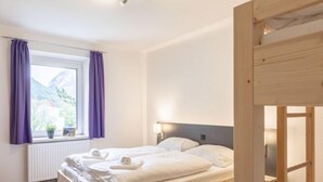 Ein Schlafzimmer mit einem hölzernen Bett, einem Fenster mit violetten Vorhängen, einem Nachttisch und Blick auf Berge.