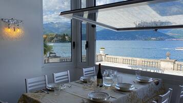 Zona pranzo con tavolo apparecchiato per quattro, vista su un lago, montagne e una città in lontananza.