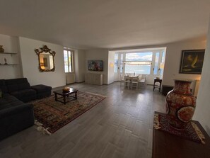 Un salon spacieux avec un canapé foncé, une table basse et un coin repas avec une table dressée pour quatre personnes.