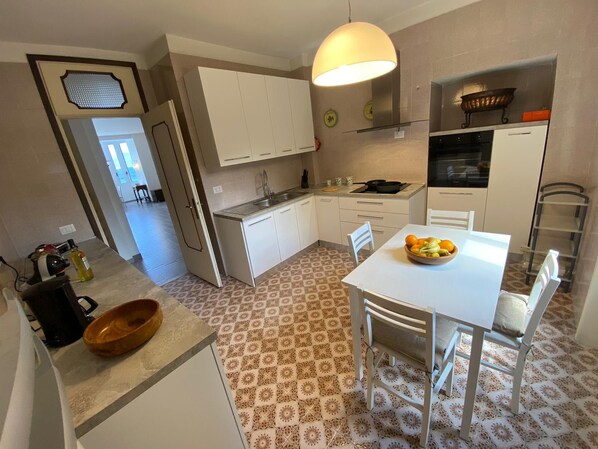 Una cocina compacta con armarios blancos, una mesa de comedor con sillas, piso estampado y una lámpara colgante.