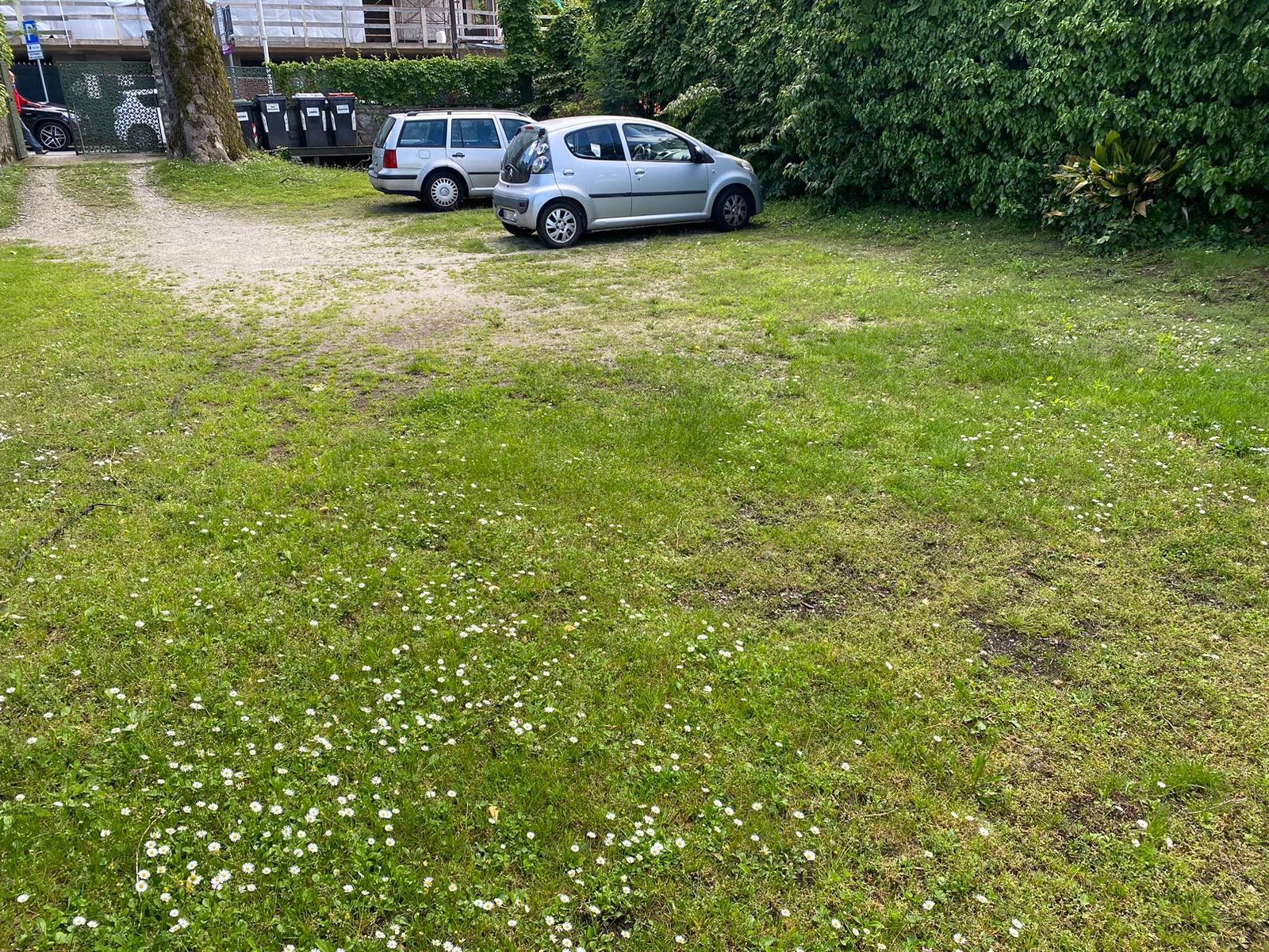 Une zone herbeuse avec des voitures garées et un bâtiment en arrière-plan.