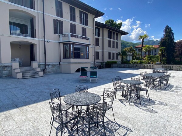 Une cour avec des sièges en plein air, un bâtiment doté de nombreux balcons et un paysage montagneux en arrière-plan.