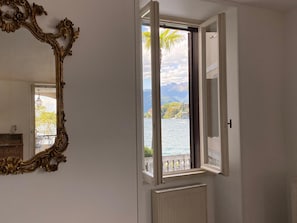 Ein Zimmer mit einem großen, verzierten Spiegel, einem Fenster mit Blick auf einen See und Berge sowie einer Heizung.