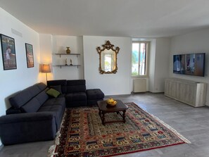 Una sala de estar con un sofá, una mesa de centro con fruta, un tapete estampado, un espejo decorativo y una televisión.