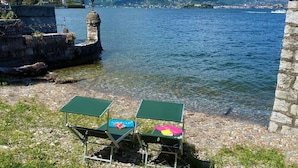 A lakeside view with a stone structure and two green tables with books. - Wonderful Stresa apartment on the lake in Stresa (Stresa)