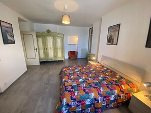 Ein Schlafzimmer mit einem farbenfrohen Bettbezug, einem Holzkopfende, einem Nachttisch, einer Lampe, einem Kleiderschrank und einem Sessel.